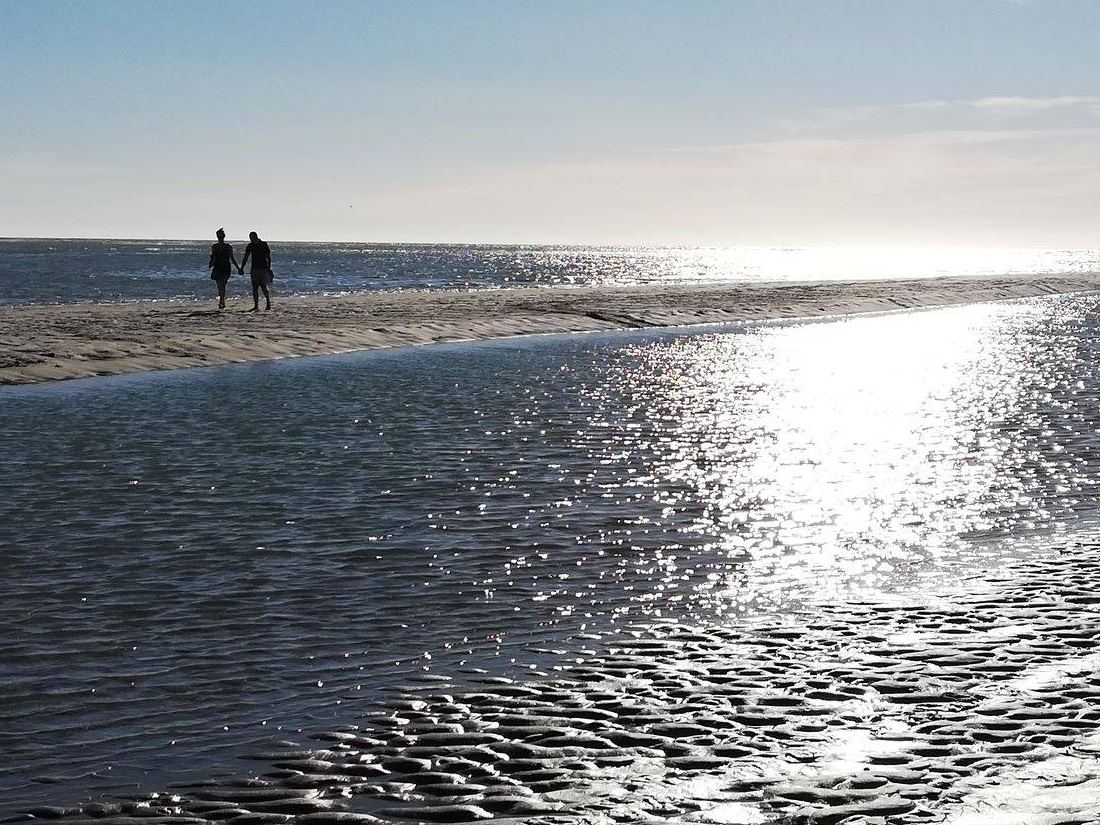 Un couple marche au bord de l’eau sur la plage de Berck à marée basse